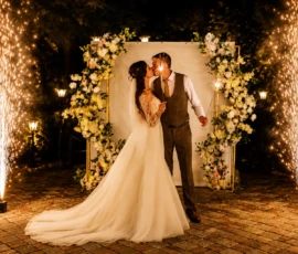 Bride and groom sharing a kiss beneath a floral arch surrounded by cold spark fountains at an Orlando wedding reception illuminated by Tyler Light.