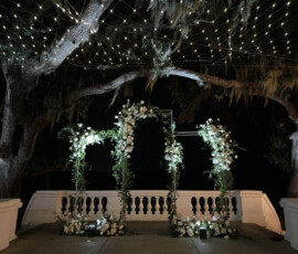 Outdoor wedding ceremony beneath warm string lights with illuminated floral structures in Orlando